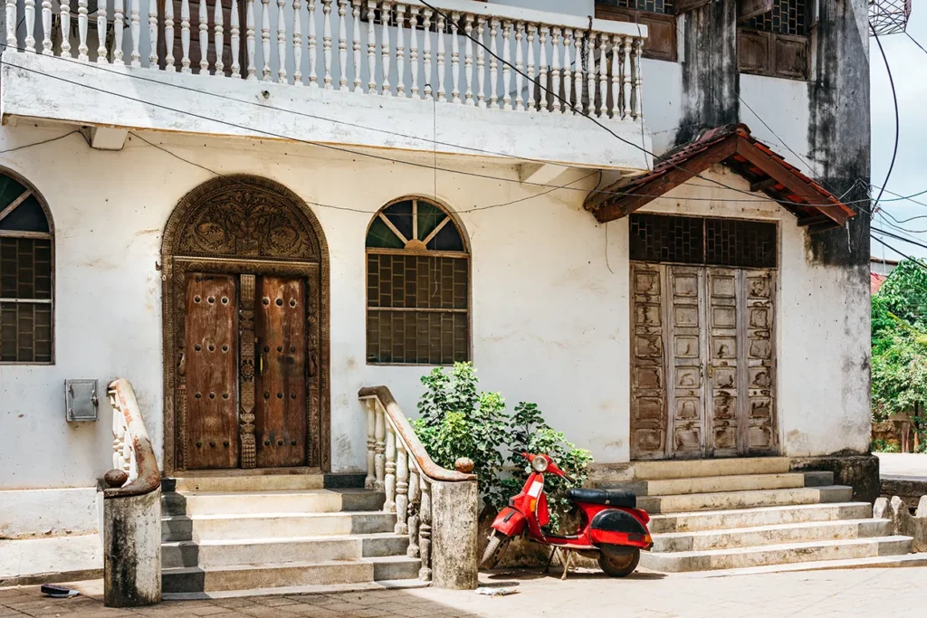 Lovely scene of wooden carved doors on a building with a scooter parked outside in Zanzibar