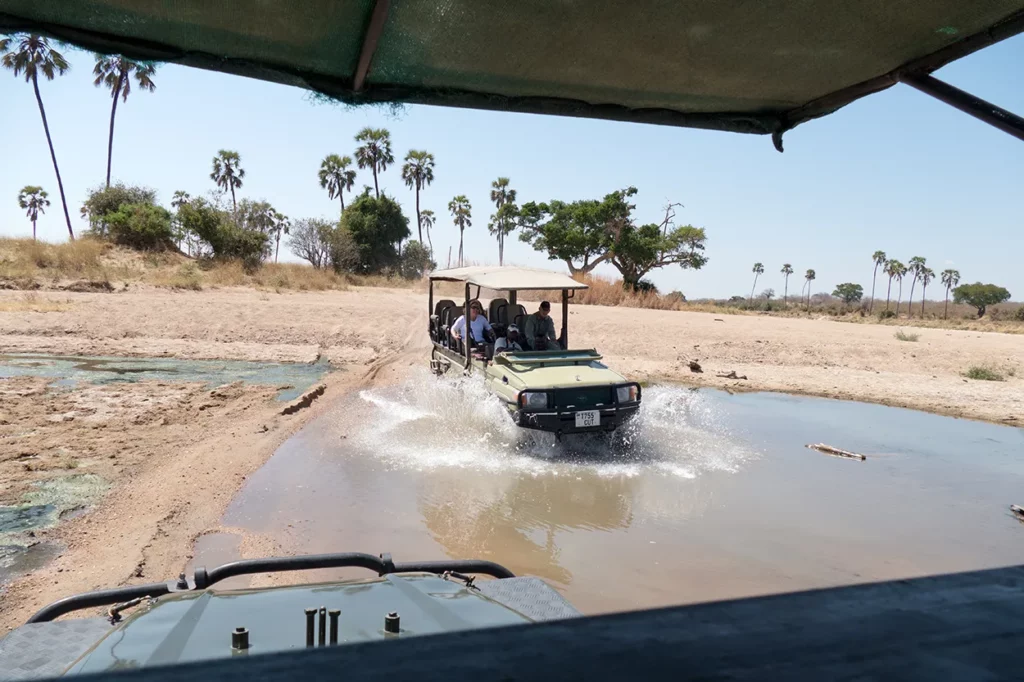 On a game drive in Ruaha game reserve, a vehicle driving through the water photographed from another vehicle